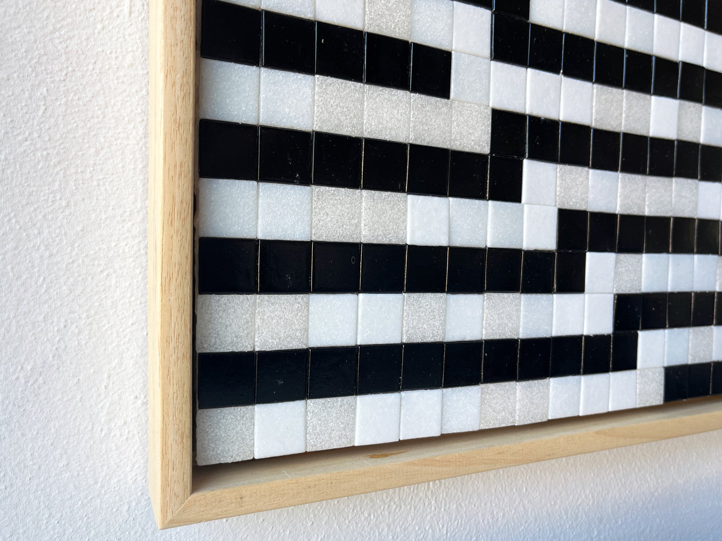 Close-up van een minimalistisch kunstwerk met zwart-witte tegels en een houten lijst