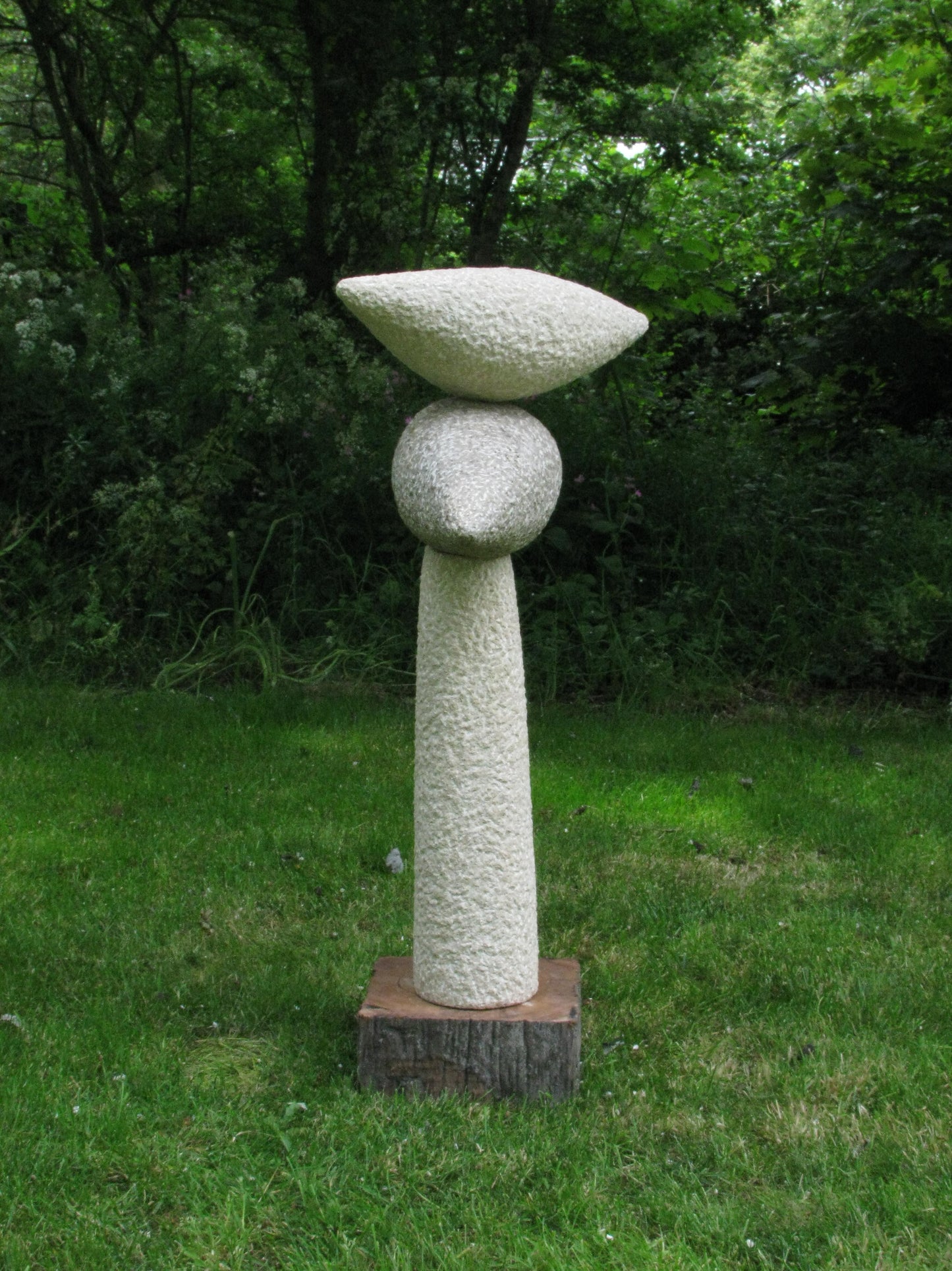 Eigentijdse steen sculptuur van Fieke de Roij met organische vormen in een groene tuin