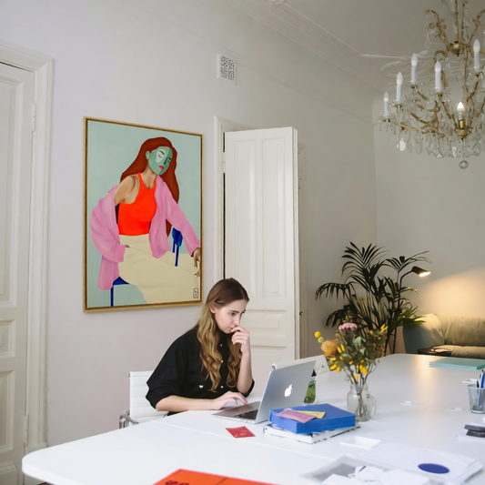 Thuiswerkplek met kunstwerk aan de muur en een vrouw die nadenkt over Is kunst belasting aftrekbaar voor bedrijven?