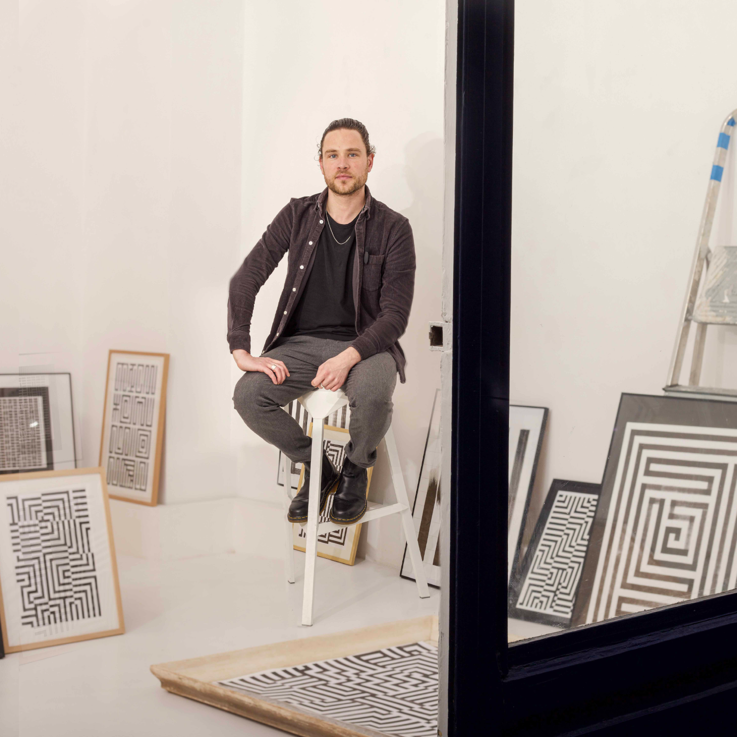 Kunstenaar poseert in witte ruimte met verschillende Guido de Boer kunstwerken rondom hem geplaatst