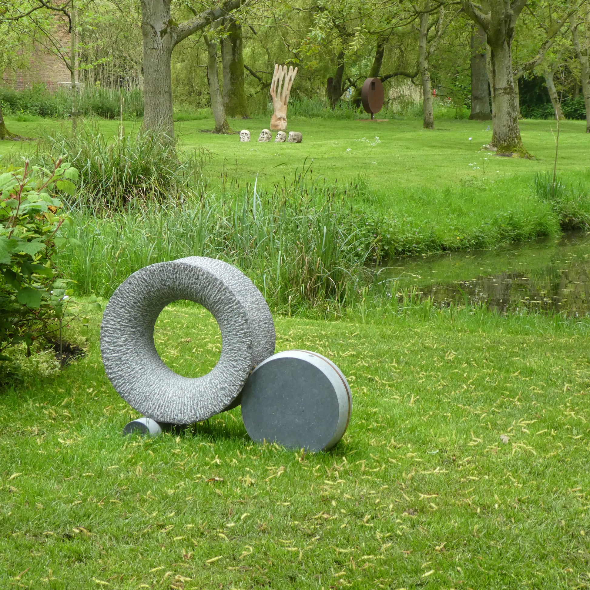 Moderne hardsteen sculptuur met cirkelvormige elementen in een groen parklandschap
