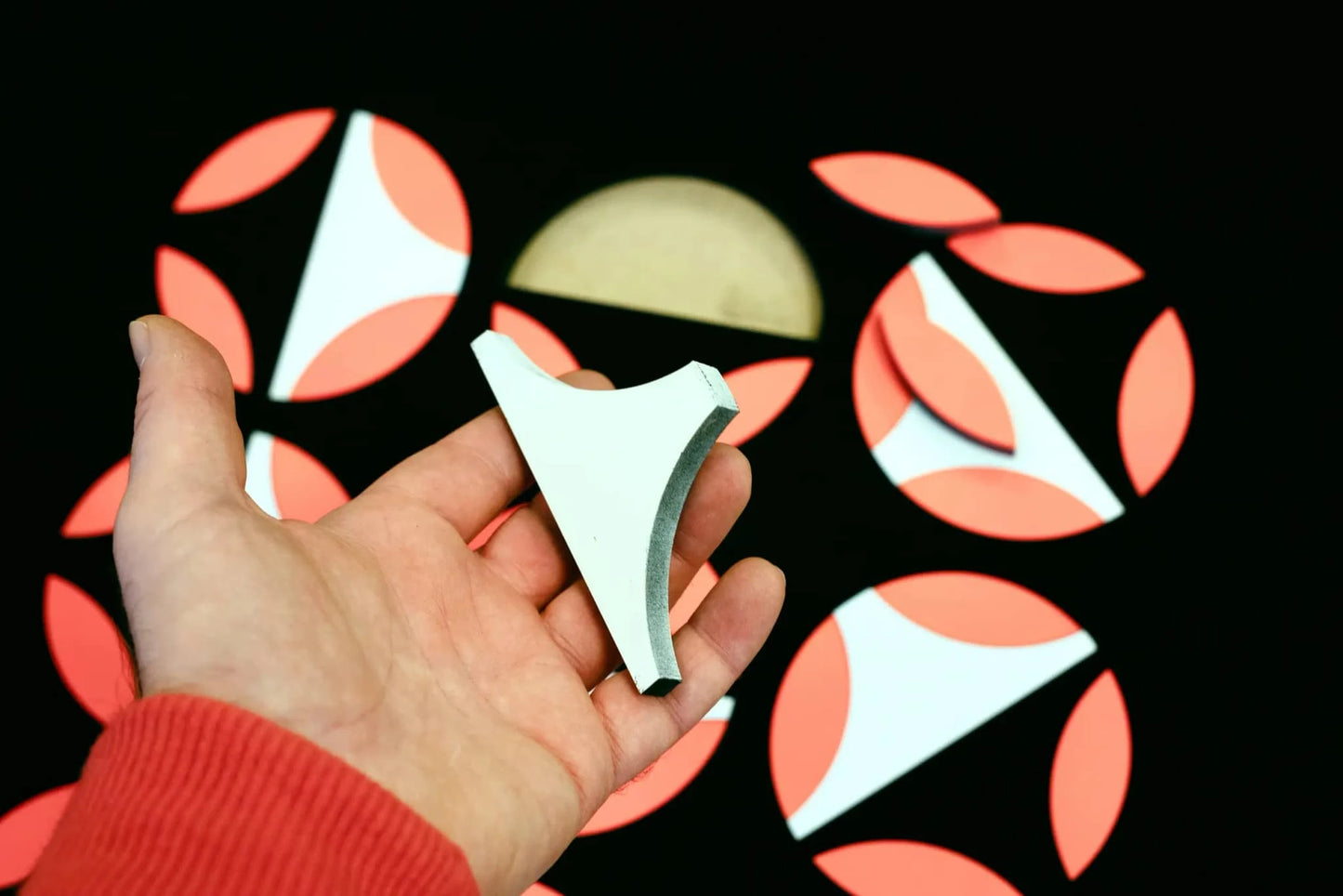 Hand houdt een stuk moderne wanddecoratie vast met geometrische vormen en levendige kleuren