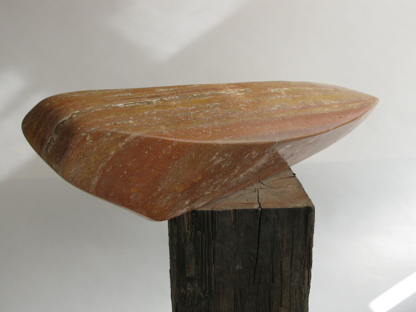 Unieke travertijn sculptuur van Fieke de Roij op een houten voet, met een organische vorm en warme kleuren