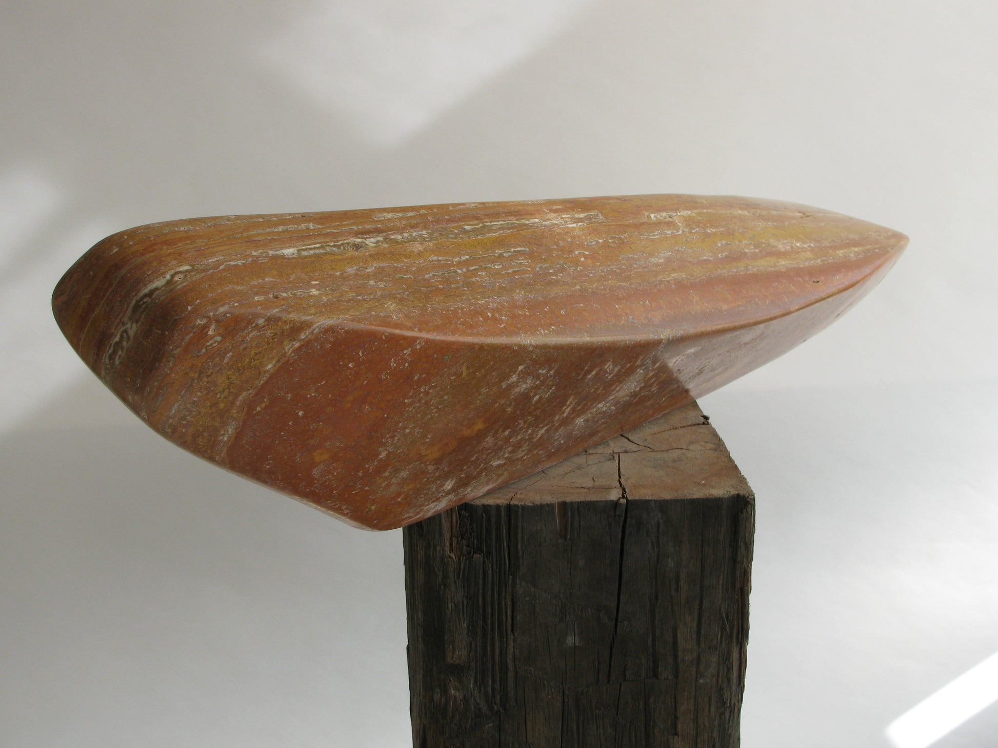 Unieke travertijn sculptuur van Fieke de Roij op een houten voet, met een organische vorm en warme kleuren