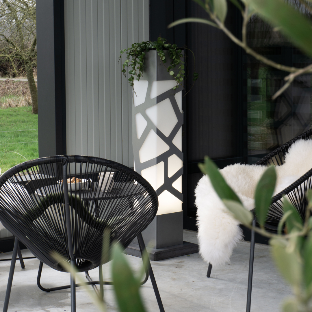 Moderne tuinlamp Linea Tree Gold van Dislux geplaatst op een patio naast zwarte stoelen